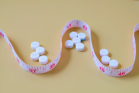 A measuring tape and pills lying on color background.