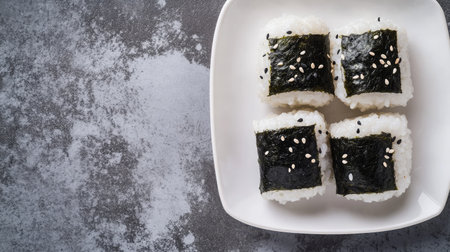 Freshly made onigiri (rice balls) with seaweed wrapping, arranged on a white plate with space for text.の素材