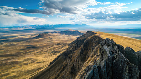 Aerial shot of a mountain ridge and expansive plains below, with open sky for text insertionの素材