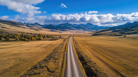 Top view of a solitary road running through a vast mountain landscape, with ample space in the open fields and sky for copy.の素材
