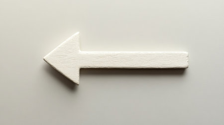 A simple white wooden arrow sign pointing left, set against a neutral background, perfect for illustrating direction and guidance in various creative projects.の素材