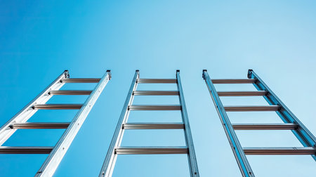 A striking image featuring three metal ladders reaching up into a bright blue sky, representing themes of growth, ambition, and the pursuit of success in everyday projects.の素材