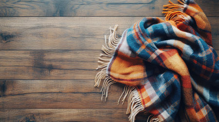 This image showcases a vibrant flannel blanket in orange and blue hues, artistically arranged on a wooden surface, perfect for capturing seasonal comfort and warmth.の素材