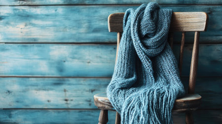 A soft blue knitted scarf gracefully drapes over a rustic wooden chair, set against a distressed blue background. Ideal for capturing warmth and comfort in home decor.の素材