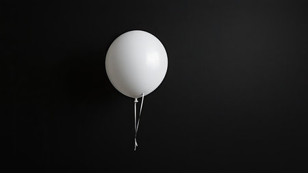 A minimalist image featuring a single white balloon hanging against a dark background, perfect for conveying simplicity and elegance in design.の素材