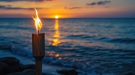 A wooden torch stands lit on the shore, the ocean reflecting hues of the setting sunの素材