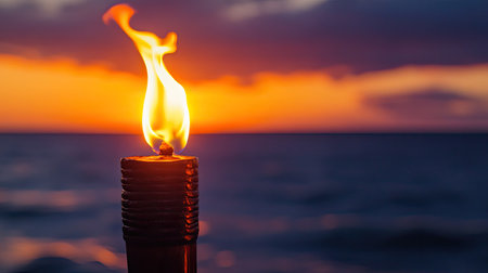 Close-up of a tiki torch glowing warmly as the sun dips below the horizon over the seaの素材