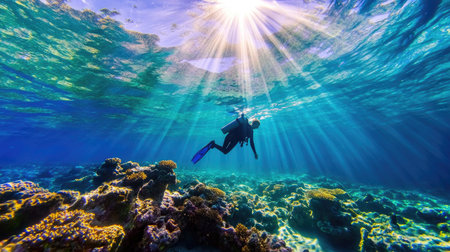A diver swims gracefully through a vibrant coral reef, illuminated by sunbeams piercing the clear ocean water, showcasing the beauty of marine life.の素材