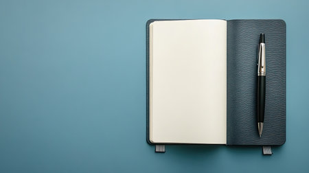 A stylish notebook lies open with blank pages alongside a sleek pen. The minimalist design on a blue background creates an inviting workspace for inspiration and creativity.の素材