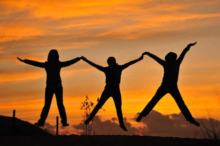 silhouette of friends jumping in sunsetの写真素材
