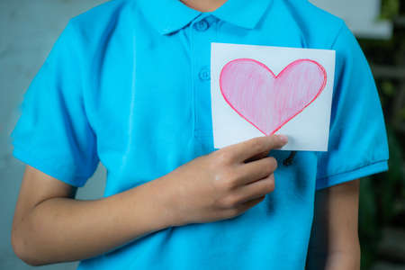 Boy holding a pink paper heartの写真素材