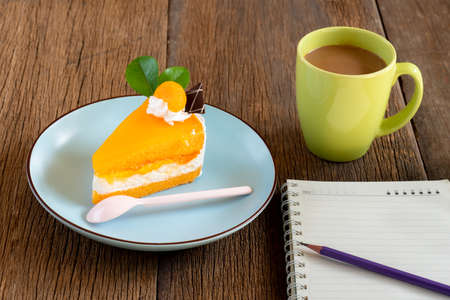 Orange cake and Coffee on wooden background ,Orange cake on a blue plate ,Coffee in green cup ,  Notebooks and pencils on wooden tablesの写真素材
