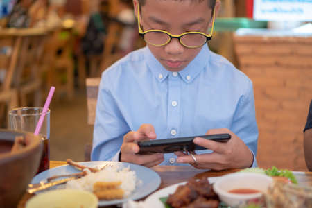 The boys are playing the phone when eating dinner.の写真素材