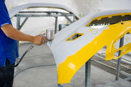 Man with protective clothes and mask painting car using spray compressor ,yellow front bumperの写真素材