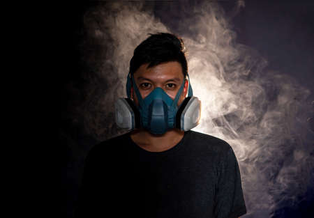 man in a gas mask smokes and breathes a cloud of tobacco smoke ,black backgroundの写真素材