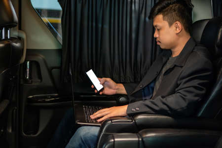 Smart young businessman using laptop and mobile in luxury automobile, working ,の写真素材