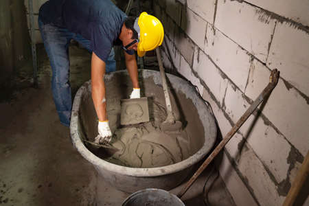 Plasterer in blue working uniform plastering the wall indoors ,Plasterer putting plaster on wallの写真素材