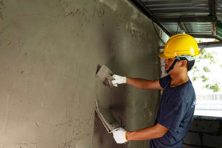 Plasterer in blue working uniform plastering the wall indoors ,Plasterer putting plaster on wallの写真素材
