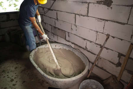 Plasterer in blue working uniform plastering the wall indoors ,Plasterer putting plaster on wallの写真素材