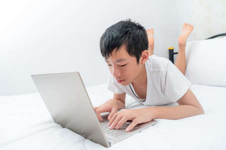 Asian boy playing social media with laptop ,On a white bedの写真素材