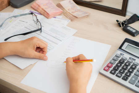 Women are collecting all expenses in the house. ,Using a pencil to collect numbers