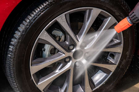Cleaning the wheels with a water gun ,Car wash using high pressure water. Detail of manual wheel cleaning concept.Red carの写真素材