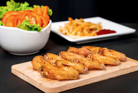fast food , french fries and fried chicken , with green salad, tomatoes on dark tableの写真素材