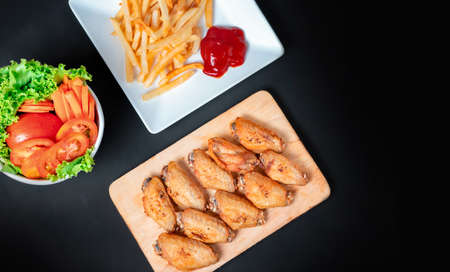 fast food , french fries and fried chicken , with green salad, tomatoes on dark table, top viewの写真素材