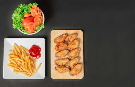 fast food , french fries and fried chicken , with green salad, tomatoes on dark table, top viewの写真素材