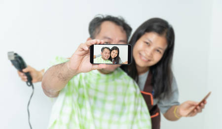 The husband and wife are taking the selfie ,While cutting his hairの写真素材
