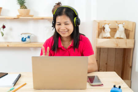 A happy, casual woman working on a laptop sitting at a desk in the houseの写真素材