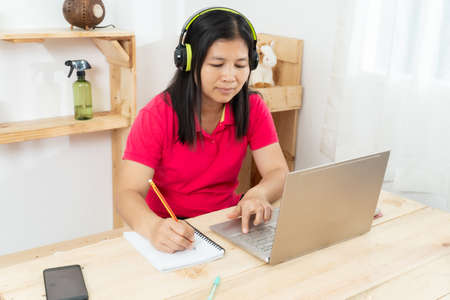 A happy, casual woman working on a laptop sitting at a desk in the house