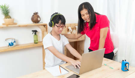 Mother is teaching her son, studying online at home. Online lesson for children. Child studying from home with the help of the mother. Work from home.の写真素材
