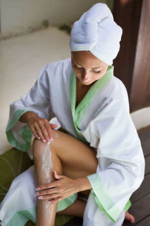 Young beautiful woman applying moisturizer to her skin after showerの写真素材