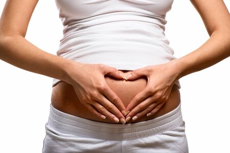 Woman holding her hands in a heart shape on her pregnant belly の写真素材