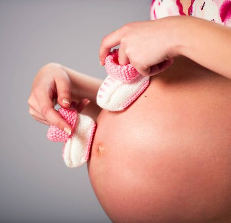 Pregnant woman holding a pair of pink baby bootiesの写真素材