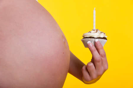 Pregnant woman belly and cake with candle in hand close-upの写真素材