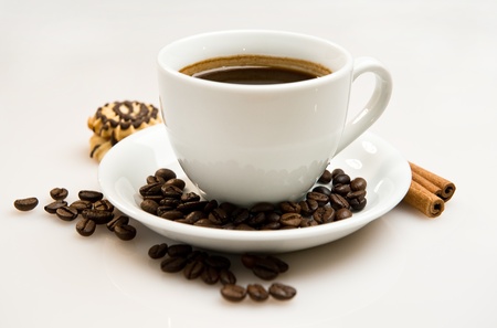 Cup of coffee with beans and cinnamon sticks over white backgroundの写真素材