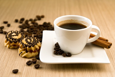 Cup of coffee with beans and cinnamon sticks over wooden backgroundの写真素材