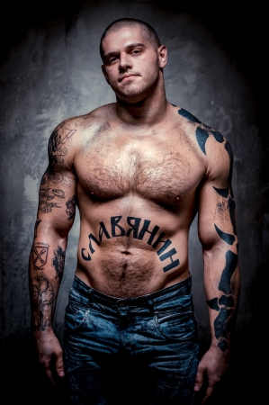 Muscular young man with many tattoos posing over grey backgroundの写真素材