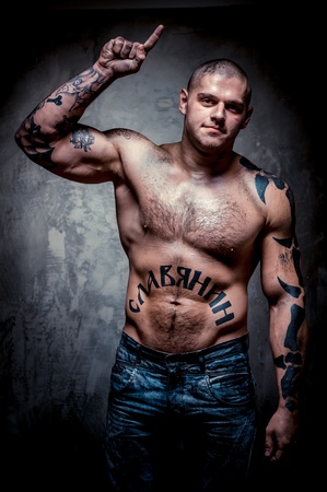 Muscular young man with many tattoos posing over grey backgroundの写真素材
