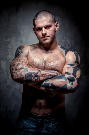 Muscular young man with many tattoos posing over grey backgroundの写真素材