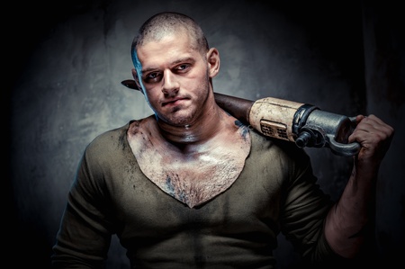 Muscular young man with jackhammer posing over grey backgroundの写真素材