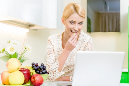 Beautiful young woman using her laptop computer in the kitchenの写真素材