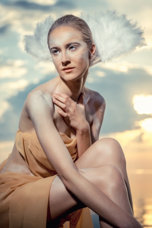 Young beautiful woman as swan posing on the beach at sunset  の写真素材