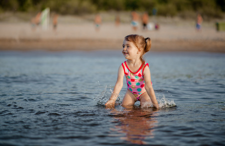 Adorable baby girl playing with a water in the seaの写真素材