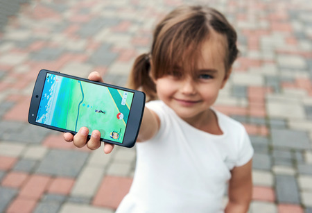 Riga, Latvia- July 17, 2016: Little girl playing a Pokemon Go game outdoors. Pokemon Go is a popular virtual reality game for mobile devices. The game allows players to capture, battle, and train virtual creatures, called Pokemon, who appear on device scrのeditorial素材