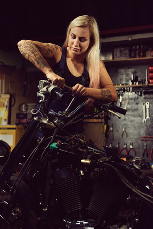Blond woman mechanic repairing a motorcycle in a workshopの写真素材