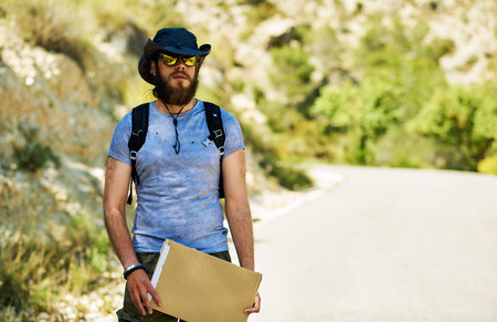 Hitch-hiking traveler with a blank cardboard sign on a mountain road. Budget travel. Auto stopの写真素材