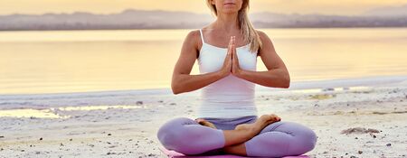 Panoramic banner middle-aged woman in activewear make namaste hands gesture sit in lotus pose during sunset sunrise do meditation on nature, balance harmony, healthy lifestyle concept panoramic imageの写真素材